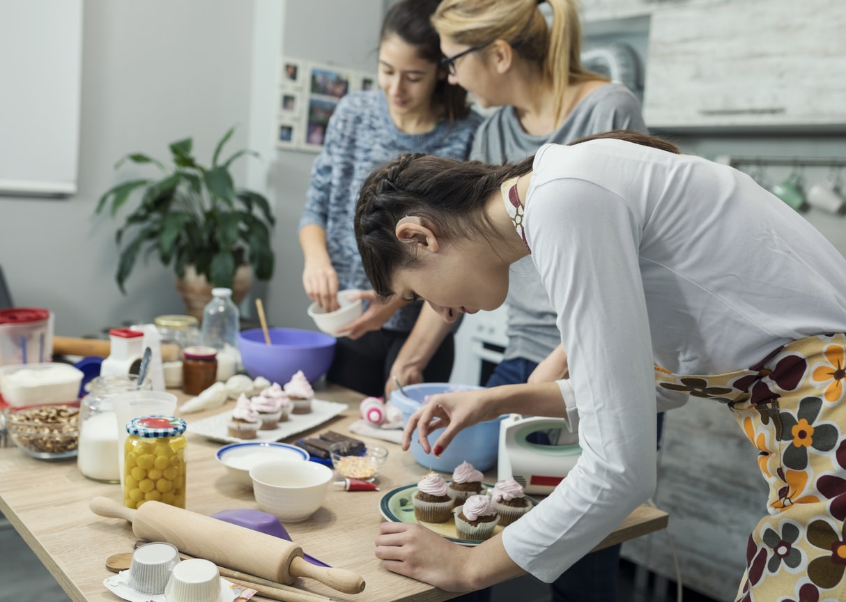 Woman with hearing aids decorating cupcakes with friends.