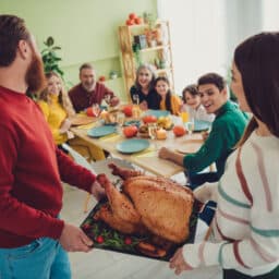 Mom and dad bringing a roast turkey to their awaiting family at the dinner table