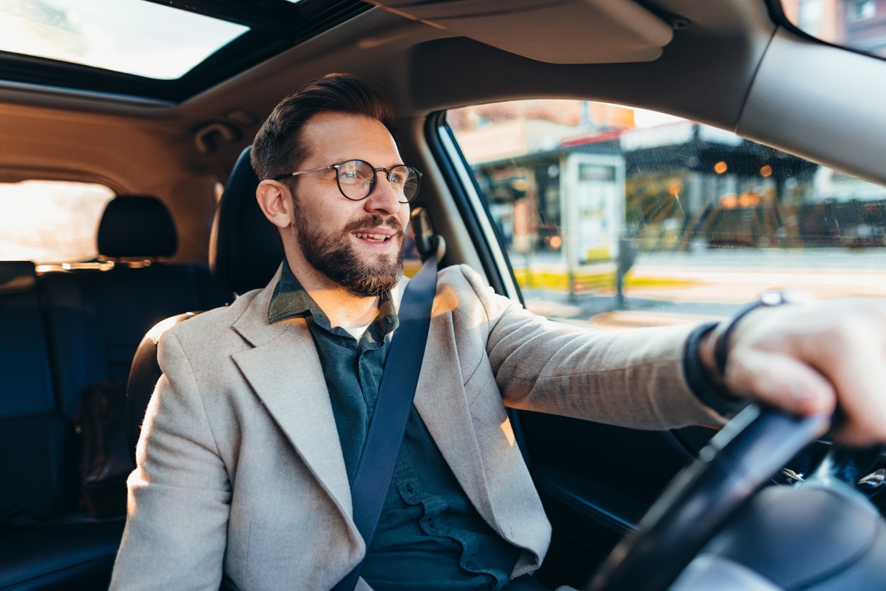 Businessman driving car in city during sunny day.
