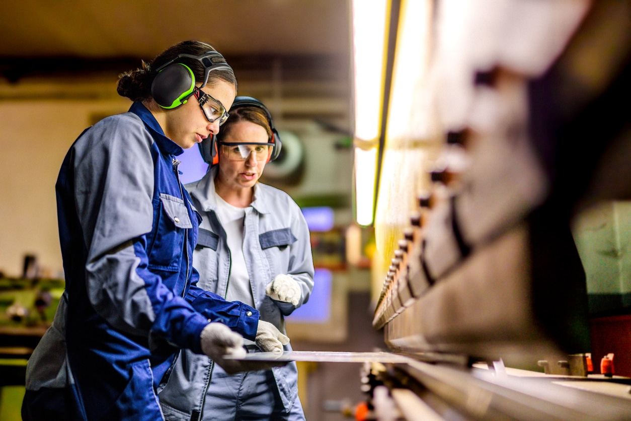 Women in safety gear use a press brake machine, working diligently in a well-lit manufacturing facility.