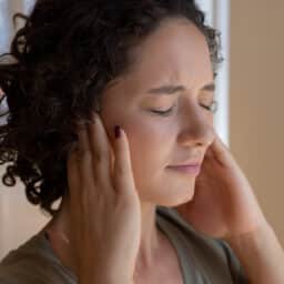 Woman holding her ears and experiencing tinnitus.