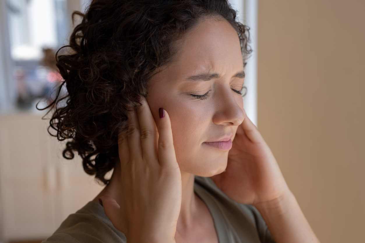 Woman holding her ears and experiencing tinnitus.