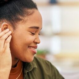 Smiling woman touching her behind-the-ear hearing aid.