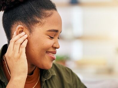 Smiling woman touching her behind-the-ear hearing aid.