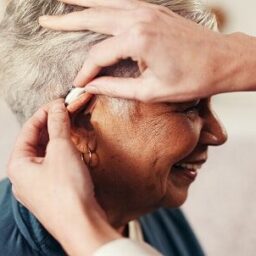 Audiologist helping a woman put on her hearing aid.