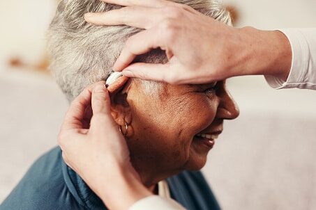 Audiologist helping a woman put on her hearing aid.