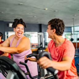 Friends talking while exercising on elliptical cross trainer at gym.