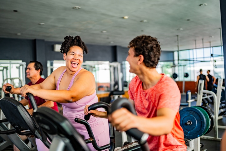 Friends talking while exercising on elliptical cross trainer at gym.